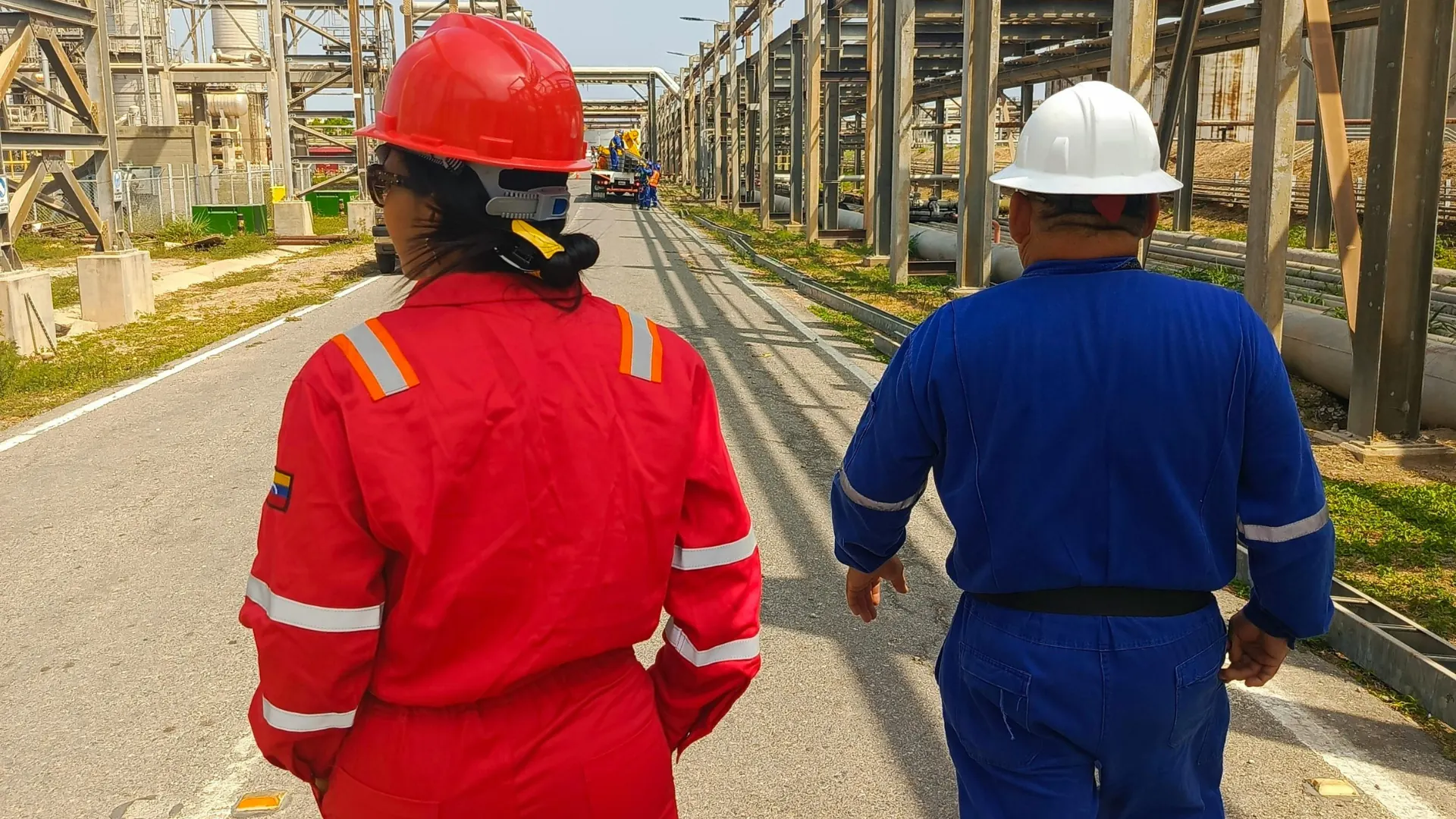 Two workers in coveralls and hard hats walking through a petrochemical plant