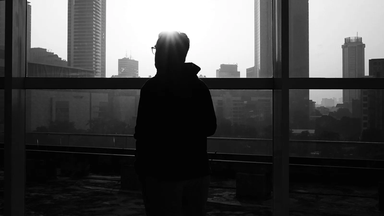 A person in silhouette at an office window overlooking a city skyline
